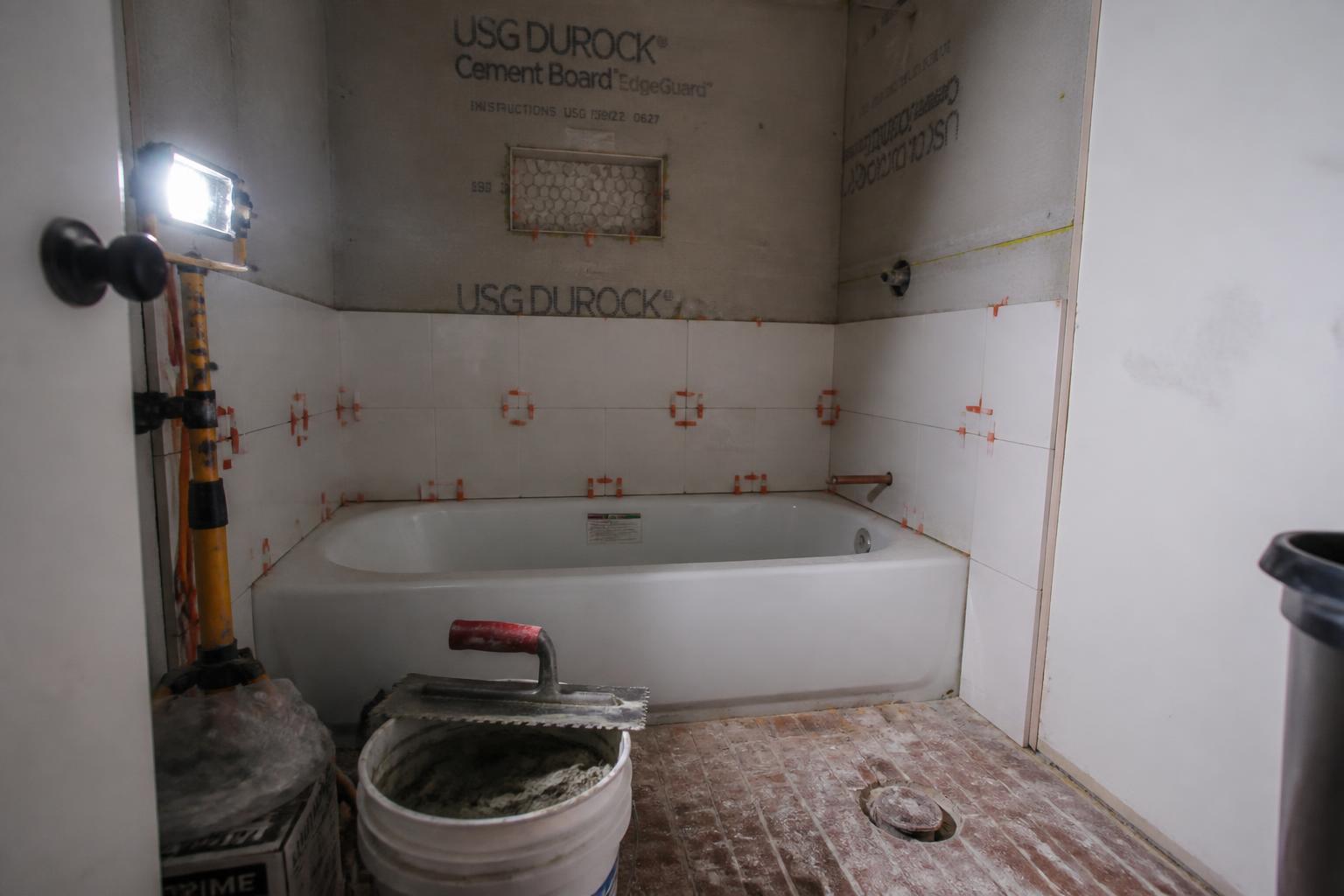 Newly remodeled American bathroom with a tiled walk-in glass shower, dark double vanity, and warm sconce lighting